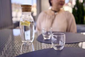 a plus size woman in peach fuzz dress chooses a dish in a restaurant via QR code in smartphone, water with lemon and glasses in front of her photo