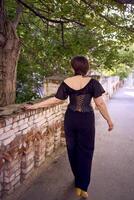 a medium size woman in a black corset and wide leg trousers walks through the city in the morning light photo