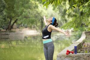 Attractive Female Breathing Fresh Air Standing Near River Side Outstretching Her Arms photo