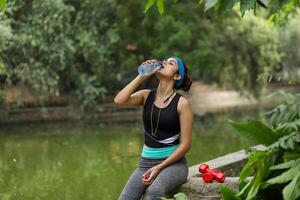 aptitud dama sentado y Bebiendo agua después ejercicio foto