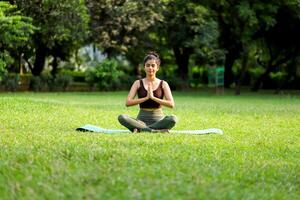 Elegant Model Sitting In Meditation Pose On Yoga Mat On Green Park photo