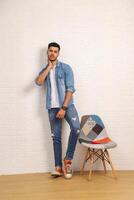 A Smart Guy Dressed In Denim Is Posing While Leaning And Resting Against The Wall photo