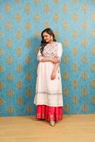 A Gorgeous Lady In An Indian Outfit Is Posing While Standing Against The Wall photo