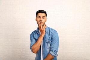 Casual Man With Surprised Face Expression Keeping His Two Fingers To The Lips photo