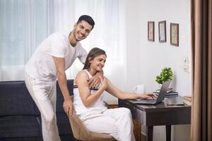 Picture Of Love Couple Sitting In Living Area Wife Working On Laptop And Husband Standing Behind Her photo