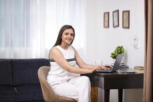 mujer mecanografía en ordenador portátil mientras posando en frente de cámara foto