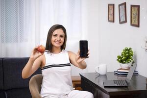 hembra nutricionista en blanco atuendo participación manzana y inteligente teléfono en mano foto
