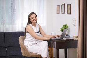 Woman Smiling While Working On Laptop Sitting On Chair In Living Room photo