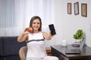 Hot Sexy Woman In White Outfit Showing Fresh Apple And Mobile Blank Screen On Camera photo