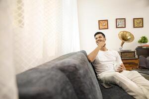 Man In White Tshirt Smiling Holding White Mug In Hand While Sitting On Sofa photo