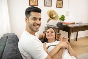 Image Of Couple In Love Sitting On Sofa And Holding Each Other Hands While Looking At Camera photo