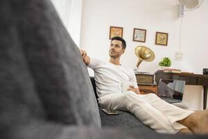 Picture Of Good Looking Man Sitting On Sofa Holding Coffee Mug In Hand photo