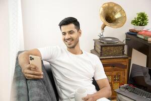 Sweet Guy Looking At His Mobile Phone Sitting In Front Of Laptop On Sofa photo