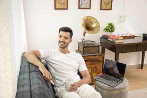 Cute Guy In His Own Thoughts Holding White Mug Sitting On Sofa photo