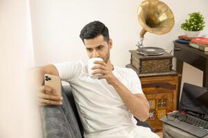 Man Using Cellphone While Drinking Coffee Sitting On Sofa photo