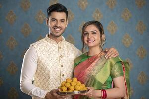 Picture Of An Adorable Couple Wearing Traditional Indian Attire Holding A Plate Of Ladoos In Their Hands And Smile photo