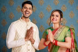 un imagen de un joven Pareja en amor vistiendo tradicional indio ropa y saludo visitantes con el namaste firmar durante el diwali celebracion foto