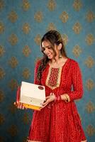 joven atractivo mujer en rojo Sharara traje participación regalo cajas en su mano durante diwali festival foto
