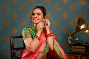 Gorgeous Lady In Saree Seated In A Chair And Touching Earrings photo