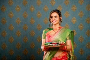 un joven, bonito ama de casa vistiendo un indio tradicional sari sostiene un puja plato durante el diwali celebracion foto