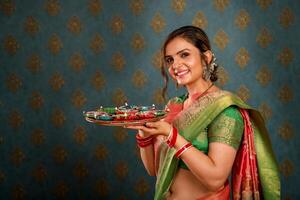 un sonriente mujer en pie vistiendo un sari y participación un pooja plato en un imagen tomado durante el diwali festival foto