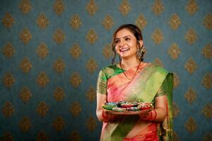 un atractivo ama de casa vestido en un antiguo indio sari y sonriendo mientras participación un pooja plato durante el festival de diwali foto