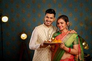 imagen de un linda Pareja celebrando diwali vistiendo tradicional indio ropa, participación un puja plato en su manos, y sonriendo foto