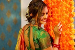 A Beautiful Girl In Saree Posing For Camera While Standing Next To The Flower-Decorated Wall photo