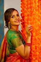 A Cute Housewife In Saree Posing Next To Flower Decorated Wall photo