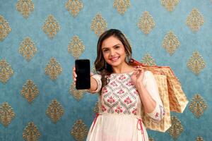 Image Of Loving Woman Holding Shopping Bags In Hand While Showing Mobile Screen On Camera photo