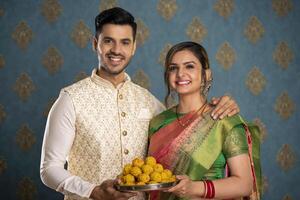 Nice Couple Holding Laddu Plate While Posing In Front Of Camera photo