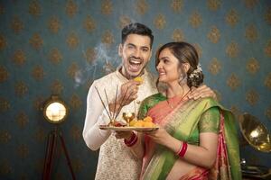 un joven Pareja disfrutando el diwali festival mientras participación un plato de laddu foto