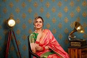 Smiling Woman In Red Saree Sitting On A Chair And Posing In Front Of The Camera photo