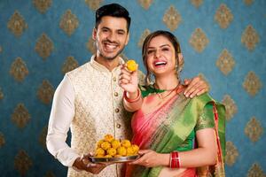 Image Of A Traditional Couple In Traditional Indian Outfits Holding A Plate Of Laddu In Their Hands And Showing A Laddu To The Camera photo