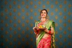 imagen de un hermosa mujer en un sari participación un plato en su mano y mirando a el cámara foto