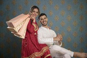 un elegante Pareja en tradicional atuendo poses con compras pantalones durante el diwali festival foto