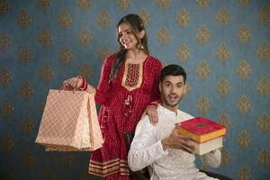 imagen de un muy hermosa Pareja celebrando diwali en tradicional ropa mientras participación regalo y dulces cajas foto