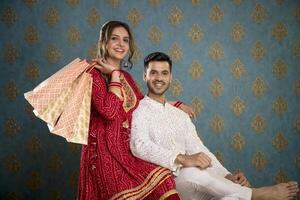 Picture Of A Lovable Couple In Traditional Indian Attire Holding Shopping Bags And Posing For The Camera While Sitting On A Sofa photo