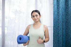 Beautiful Brunette Woman Holding Yoga Mat And Showing Thumb Up photo