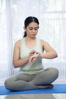 ajuste medio Envejecido mujer comprobación hora en su muñeca reloj mientras sentado en yoga estera después rutina de ejercicio foto