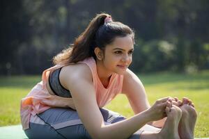 A Beautiful Blonde Woman While Sitting in the Park, Doing Yoga, and Trying to Touching Her Feet With Both Hands. photo