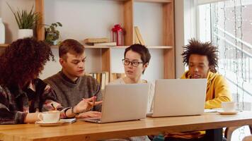 jovem corporativo multirracial colegas sentado Próximo para cada de outros às a comum mesa com laptops dentro acolhedor escritório e ativamente discutindo trabalhos projeto juntos video