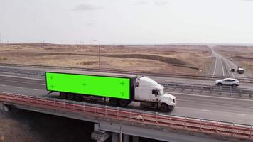 Truck with semi-trailer on which green screen passes over bridge on highway, aerial view. Truck with semi-trailer which chromakey, rides freeway. video