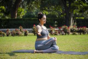 hembra aptitud instructor sentado en sentado con las piernas cruzadas yoga actitud mientras practicando ejercicio en parque. foto