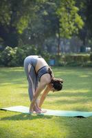 Close-up side view of a woman doing yoga in a standing forward-bending asana or yoga pose. photo