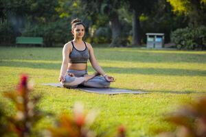 un confidente dama meditar, sentado en yoga actitud en parque. foto