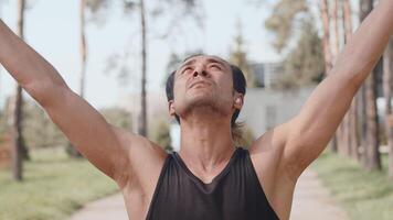 Young asian male sportsman performing warming up exercise before run and tuning up for good workout on an alley in an autumn city park on a sunny day close up video