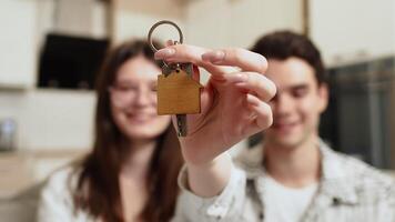 Young couple showing the keys from the new apartment, smiling and hugging each other while sitting on a couch in a cozy kitchen and looking at the camera close up video