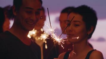 jung Mann und jung Frau Stehen mit Wunderkerzen und fröhlich reden schließen oben während ein draussen Party mit ein spektakulär Dämmerung Himmel wie ein Hintergrund. Konzept von sorglos Sommer- Spaß video