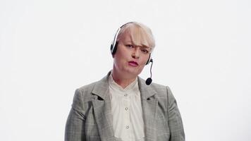 Portrait of a smiling mature caucasian woman in a headset, standing on a white background and talking with a client during a support service session video